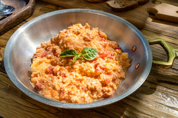 frying pan with omelette with tomatoes, decorated with fresh green basil leaves on wooden table in street cafe on sunny morning