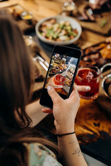 Close up of woman is making photo of meal for social networks in restaurant before dinner 