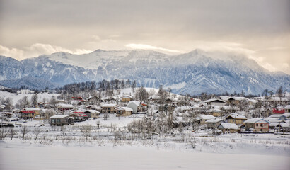 Distant view of village on hill in winter with white snow sitting on ground and houses