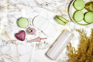 cotton pads and nail polish with macarons and daisy flowers, reeds and micellar water on marble background. Hygiene supplies, beauty tools and skin