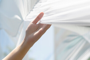 Woman hand holding white clean fabric curtain drape or clothes outdoor gently after use sunlight dry fabric after laundry. Concept of housewife washing clothes in weekend lifestyle. - obrazy, fototapety, plakaty