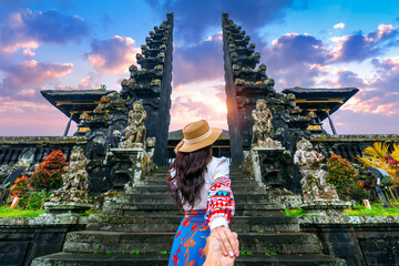 Women tourists holding man's hand and leading him to Besakih temple in Bali, Indonesia. - obrazy, fototapety, plakaty