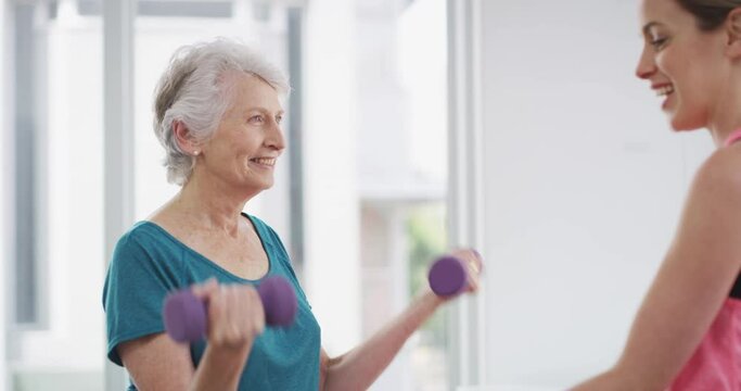Elderly, woman and coach with dumbbell for fitness, exercise or workout with communication and instructions. Senior, person and personal trainer with weight lifting, training and conversation at gym