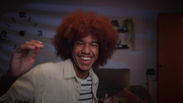 Close up handsome young afro man has fun dancing alone in living room at night. Excited Latin male influencer doing viral dance moves for social media. Generation z people enjoying free time at home. 