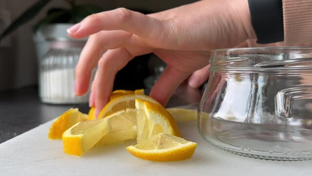 hands of woman putting lemon slices into glass jar, unrecognisable person. Close-up, slow camera movement right