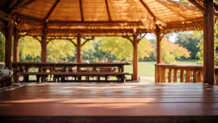 A wooden gazebo with a thatched roof in a park. The gazebo has a wooden table and benches. In the background is a blurred view of the park with trees and grass - obrazy, fototapety, plakaty