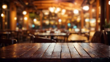 Gordijnen A wooden table in a restaurant or bar. The table is in the foreground and in the background is an area with wooden chairs and tables and pendant lights. The background is blurred © Rysak