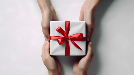 Hands giving and receiving christmas gift box on a white background. Luxury wrapped present with red color ribbon and bow. Isolated, aesthetic and minimalist. - obrazy, fototapety, plakaty