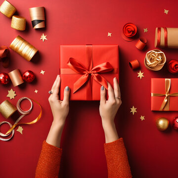Close up of hands wrapping a gift with wrapping paper on a red background.