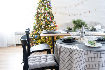 Serving a festive table with plates, forks, knives, napkins, glasses close-up in the modern interior of a loft house decorated for Christmas and New Year. Waiting for guests for a festive dinner