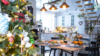 Festive interior of house is decorated for Christmas and New Year in loft style with black stove, fireplace, Christmas tree. Warm studio room with set table, burning wood, cozy and heating of home