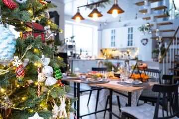 Festive interior of house is decorated for Christmas and New Year in loft style with black stove, fireplace, Christmas tree. Warm studio room with set table, burning wood, cozy and heating of home