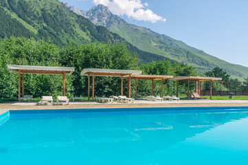 A heated swimming pool high in the mountains. Relaxing by the water in the fresh air. Sun loungers for relaxation and sunbathing near the pool. Vacation in the mountains in summer.