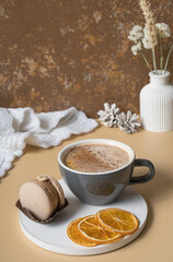 A cup of warm orange cocoa with a macaroon and cozy winter decor. Autumn winter still life with a warm drink