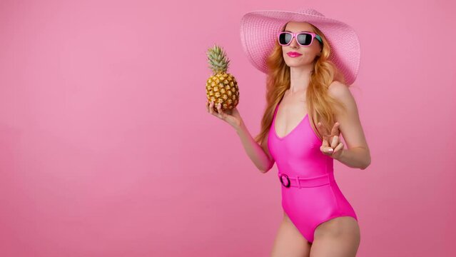 Fashionable woman dancing in swimsuit, total pink, hat with pineapple, smiling enjoys summertime for spa and wellness. Playful glamor sexy lady dance, slim body for pool party, colorful trend on pink