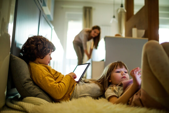 Little kids using the tablet while mom cooks dinner
