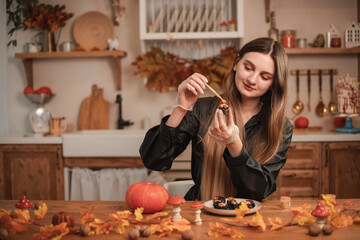 Woman confectioner decorates candy in the form of black skulls for Halloween with gold. The process of creating candies for Halloween