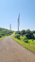 portrait view of landscape with wind turbines on both side of road with blue sky and green field