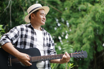 Handsome Asian man is playing acoustic guitar in the park, outdoor nature background. Concept, love...