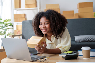 African American business woman working at warehouse preparing SME package box for delivery at small business home office.