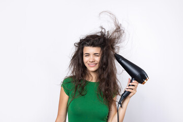 A cute young girl dressed in a green top dries her beautiful long silky hair with a hair dryer...