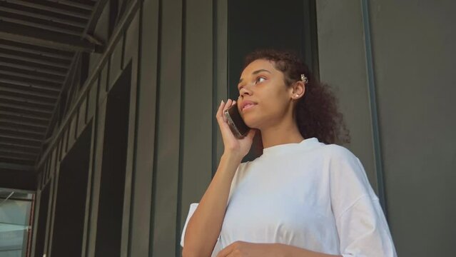 Young adult african american girl with smile on face hold mobile phone, answer to call and talk to friends, smiling and laughing. Teenager having conversation online, using gadget