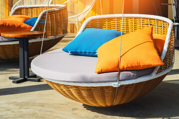 Colourful pillows on modern daybed. Brown rattan loungers with orange and blue pillows hanging with...