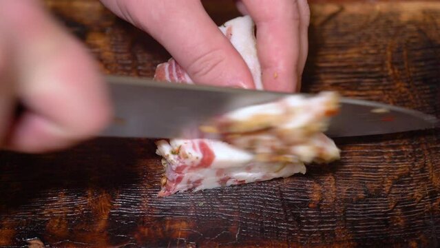 Slicing of salted pork fatback on cutting board, close-up. Ukrainian traditional food - salo	
