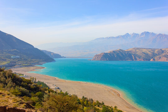 View of the Charvak reservoir from the shore. Autumn landscape of Uzbekistan: a bright blue lake and yellowed grass.