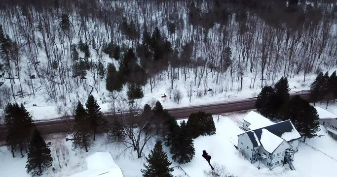 Aerial Panning Shot Of People Riding Snowmobiles During Winter, Drone Ascending Over Houses And Trees - Houghton, Michigan