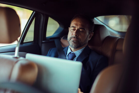 Businessman reviewing work on his laptop in the backseat of a car