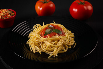 Spaghetti with sauce on a black plate in a darker studio photo.