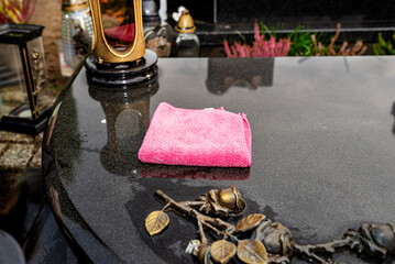 Cleaning a black tombstone with a cloth and water at a cemetery in Poland, visible pink cloth.