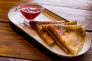 Pancakes with berry jam sprinkled with sugar on a plate on a wooden table
