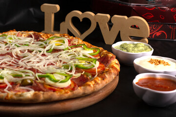 Pizza on a black background with kitchen utensils and ingredients around it, in a studio shot with a black background