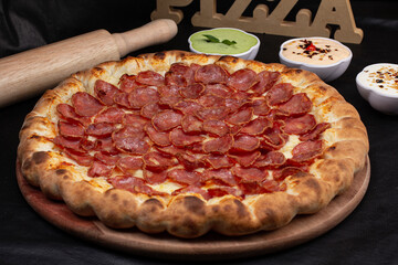 Pizza on a black background with kitchen utensils and ingredients around it, in a studio shot with a black background