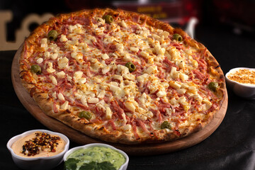 Pizza on a black background with kitchen utensils and ingredients around it, in a studio shot with a black background