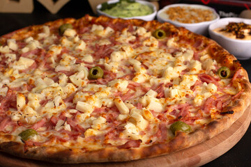 Pizza on a black background with kitchen utensils and ingredients around it, in a studio shot with a black background