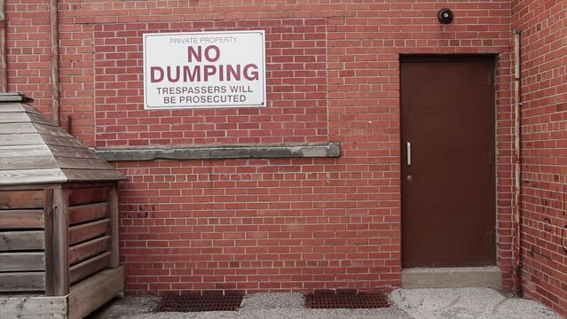 private property no dumping trespassers will be prosecuted horizontal rectangle sign on brick wall next to brown metal door, red white