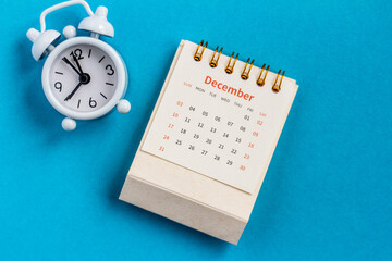 December monthly desk calendar for 2023 and alarm clock on a blue background.