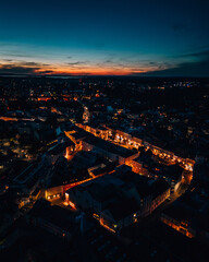 Aerial view of a town with a vibrant inner city lit up at night with a colorful sunset in the sky - obrazy, fototapety, plakaty
