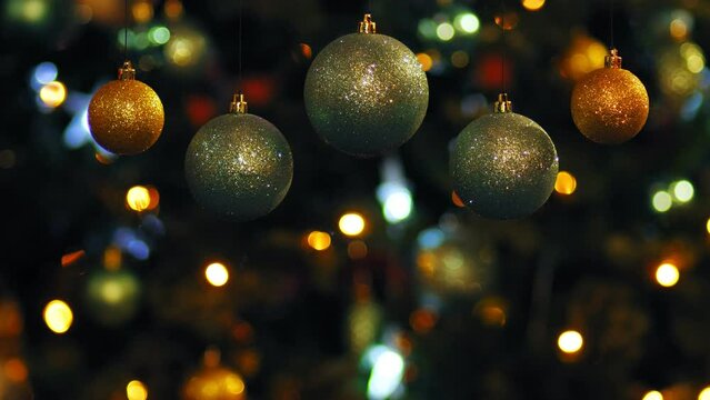 Gold and silver Christmas balls rotate against the background of luminous garlands on a Christmas tree in blur. Medium plan