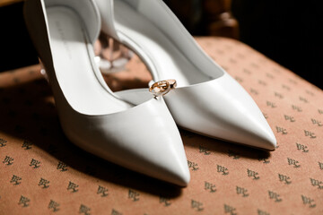 White heels with a golden ring atop, on patterned fabric. Close-up with a soft-focus background,...