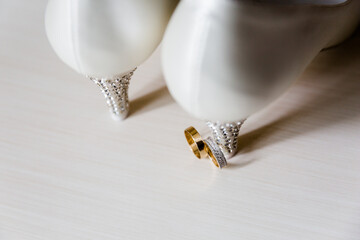 Close-up of crystal-embellished white shoe tip and a diamond half-encrusted gold wedding band on a...