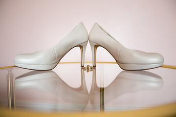 Elegant ivory heels on a clear surface with wedding bands, set against a soft pink background.