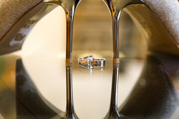 Close-up of two wedding rings nestled between glittery high-heeled shoes, reflecting a blend of...
