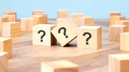 three wooden cubes with question marks over a blue background with copy space