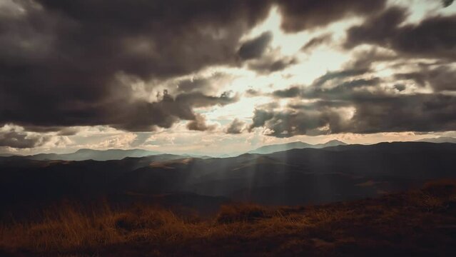 Dark dramatic autumn mountain cloudscape. Epic storm clouds moving fast, rays of rising sun break through the clouds hit the orange meadow. Vintage dark sunset footage time lapse. Nature background