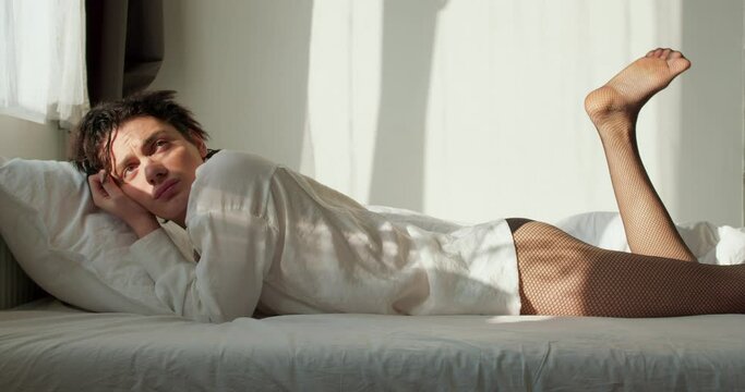 young careless relaxed lazy handsome transgender man lying in bed raising legs after waking up in morning at home slow motion Life without problems