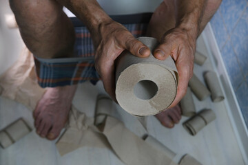 man suffering from diarrhea holds roll of toilet paper while sitting on toilet, gastrointestinal...